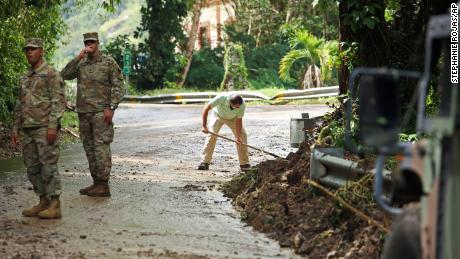 توجه قوات الحرس الوطني حركة المرور حيث يساعد المقيم لويس نوجويرا في إخلاء طريق تضرر من إعصار فيونا في كايي ، بورتوريكو ، يوم الثلاثاء.